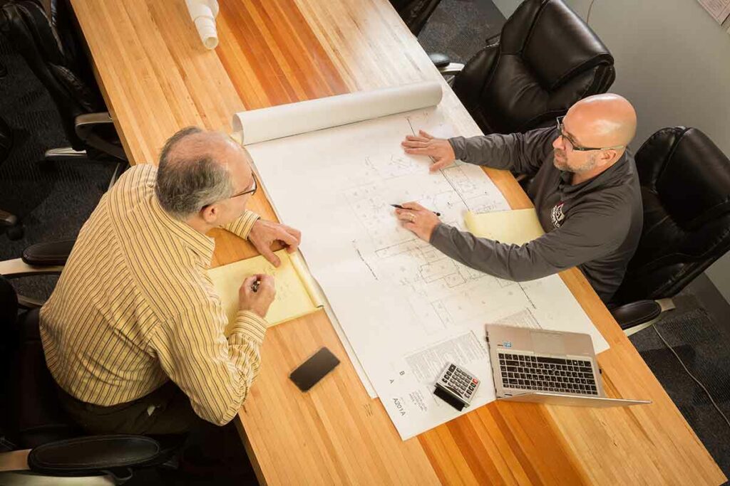 two men reviewing plans on a wood table