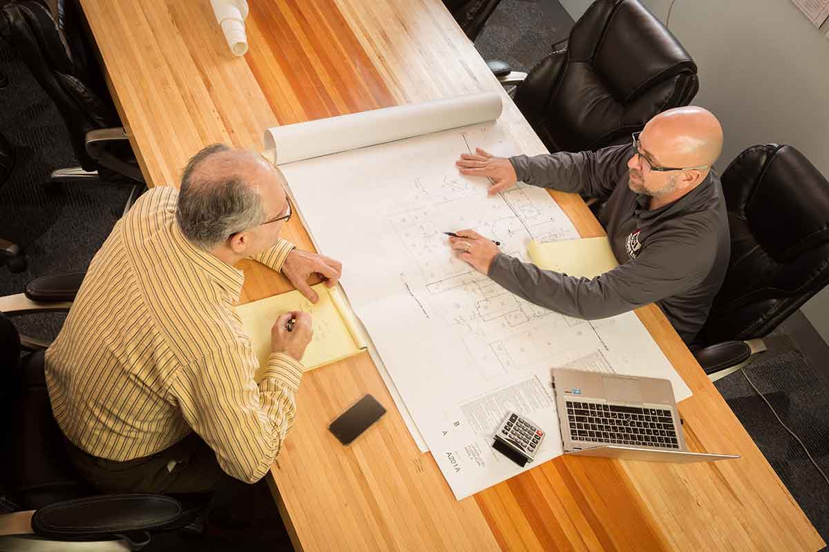 two men reviewing plans on a wood table