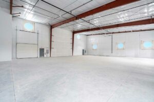 large space with bare concrete floor, ted metal support beams, white walls, and round windows.