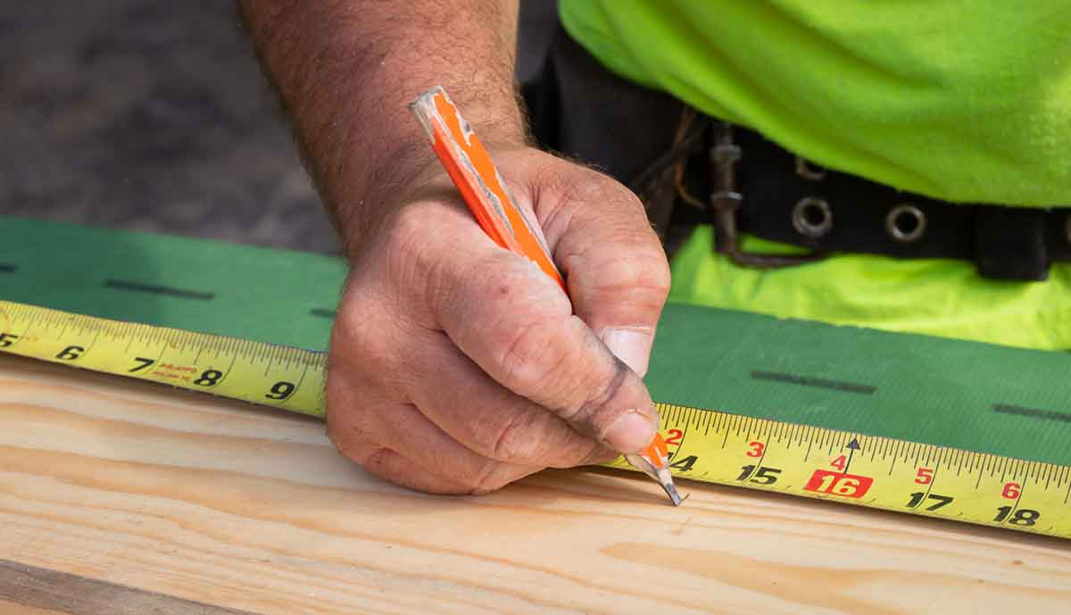 Hand holding pencil marking wood next to tape measure