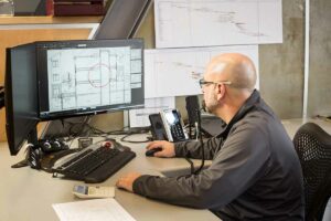 Man in gray fleece looking at plans on a computer monitor