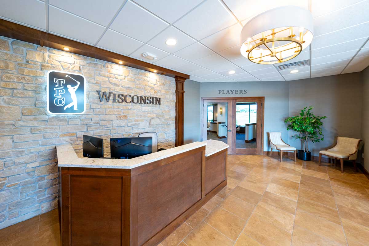 reception area with brown wood desk in front of stone wall with TPC Wisconsin signage, doors to Players in background